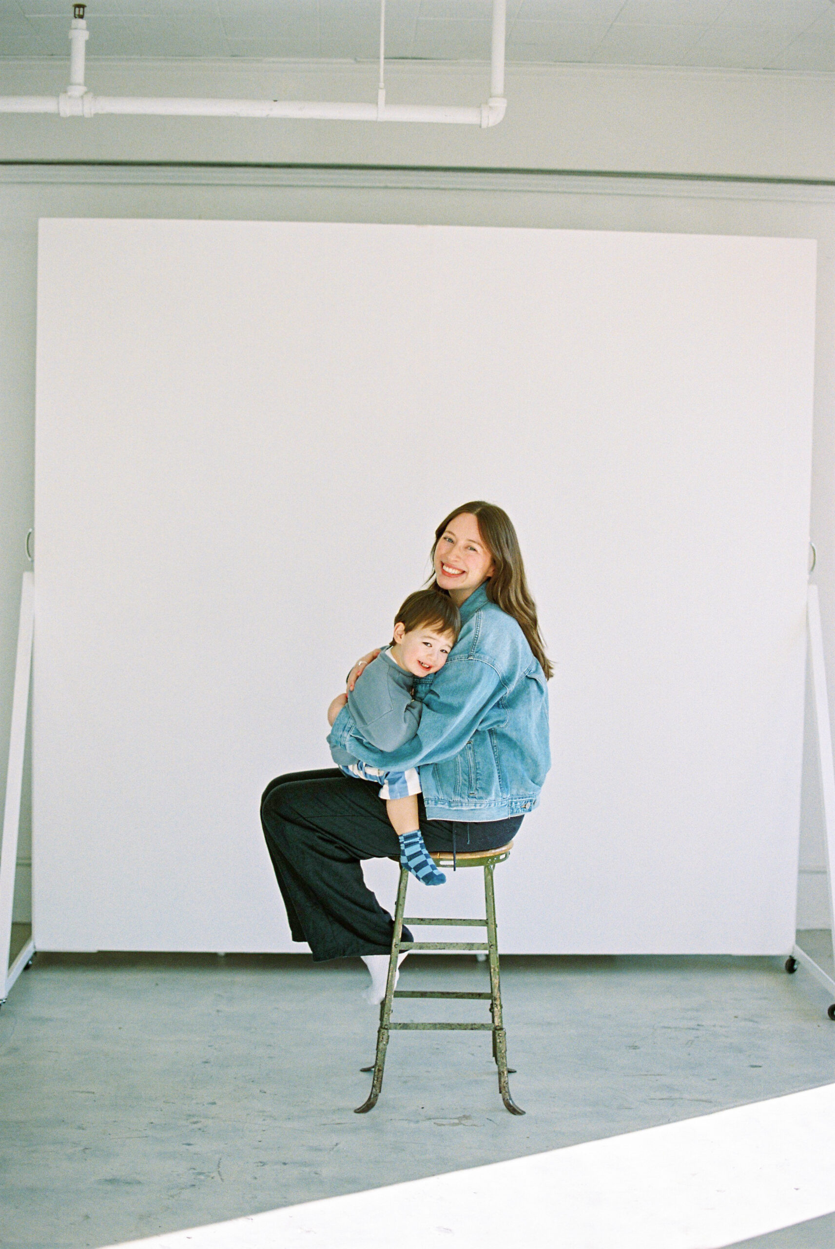 Pregnant mom and her toddler son sitting on a high chair for a portrait in a studio in Vancouver
